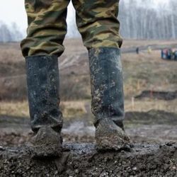 在泥泞的田野里，一双穿着迷彩服的腿站在一双泥泞的靴子里。